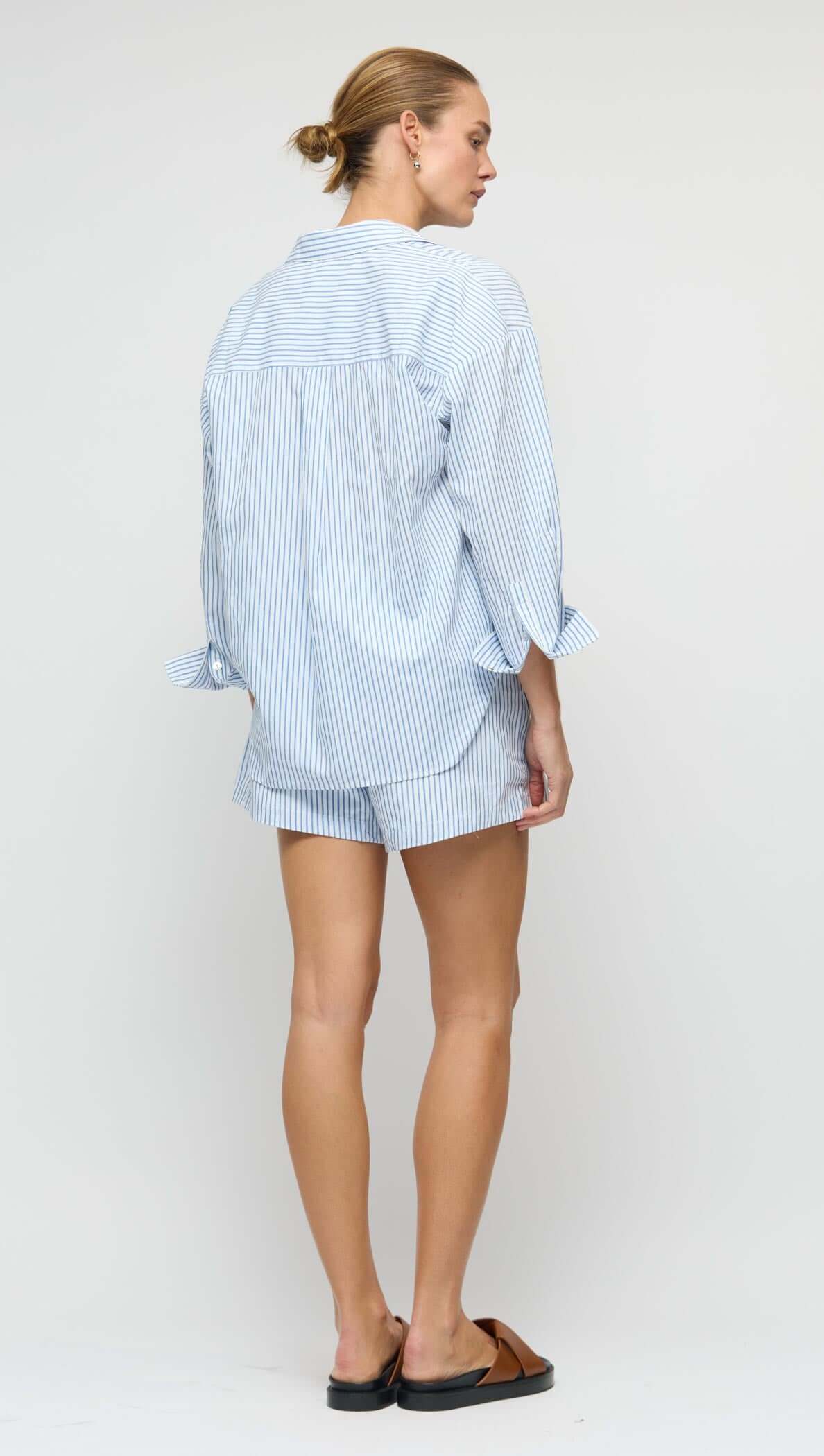Woman wearing a Cotton Blue & White Oversized Shirt with shorts, showcasing the relaxed fit and classic stripes.