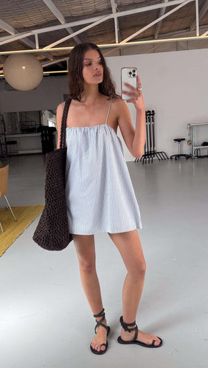 Woman modeling a Cotton Blue & White Stripe Mini Dress with adjustable straps and a stylish bag.