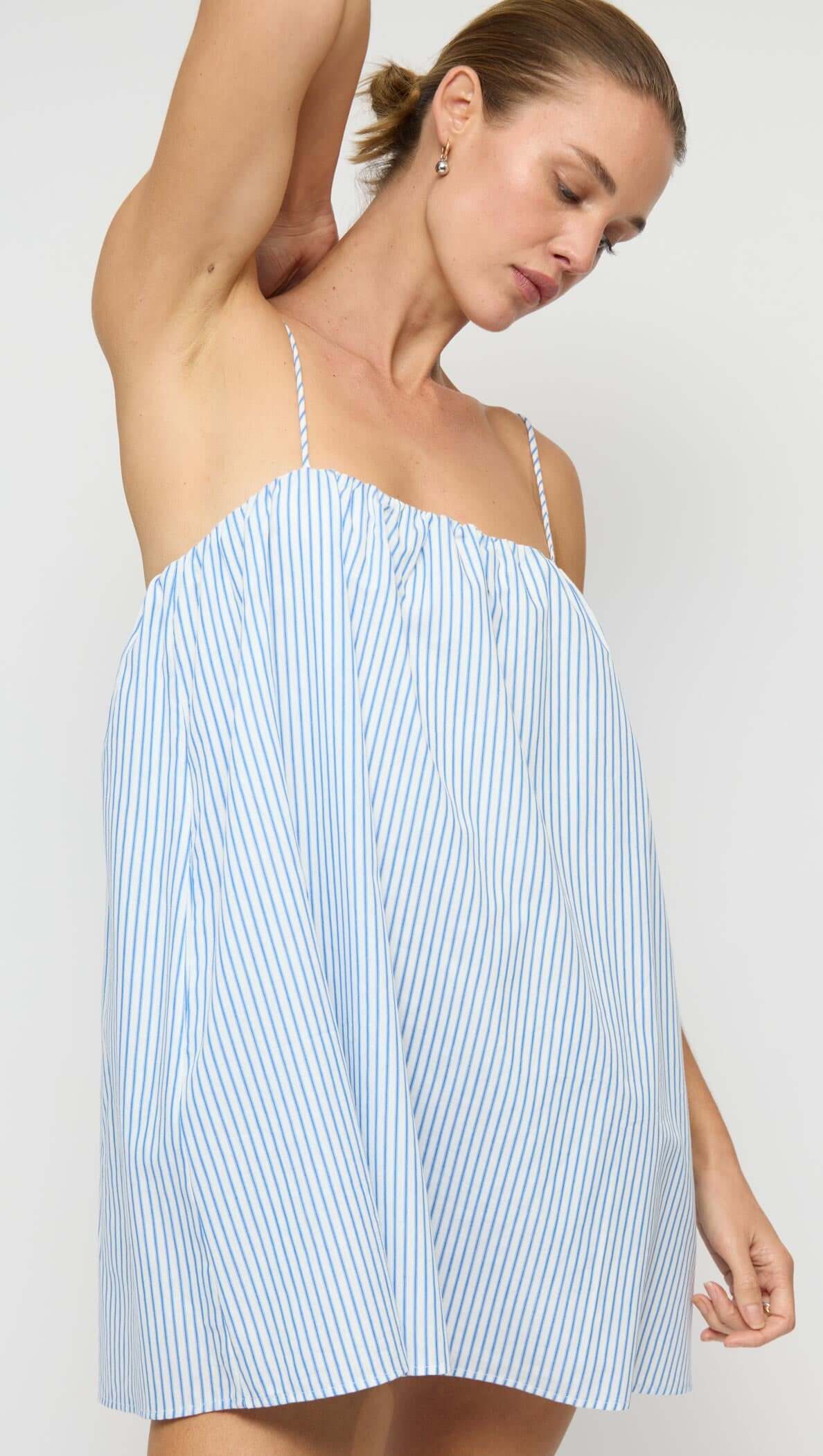 Cotton Blue & White Stripe Mini Dress worn by a model, showcasing its relaxed trapeze silhouette and adjustable tie-back straps.