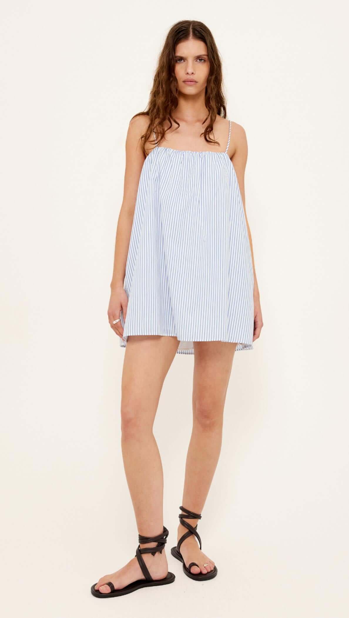 Cotton Blue & White Stripe Mini Dress displayed on a model, featuring a relaxed trapeze silhouette and adjustable tie-back straps.