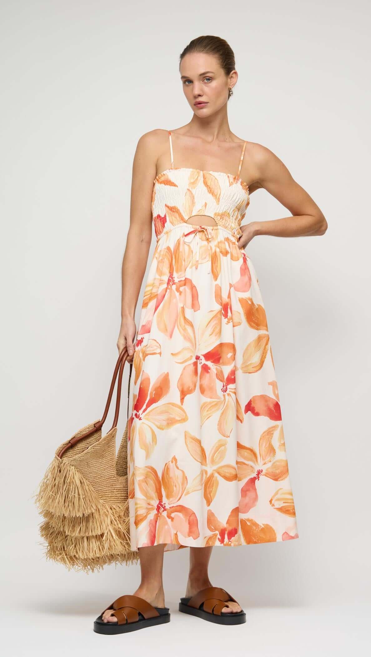 Model wearing an Orange & White Floral Shirred Midi Dress, styled with a straw bag and sandals.