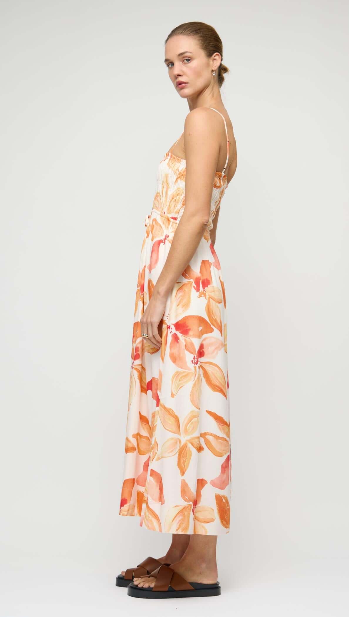 Side view of model wearing the Orange & White Floral Shirred Midi Dress with a flowing skirt and floral print.