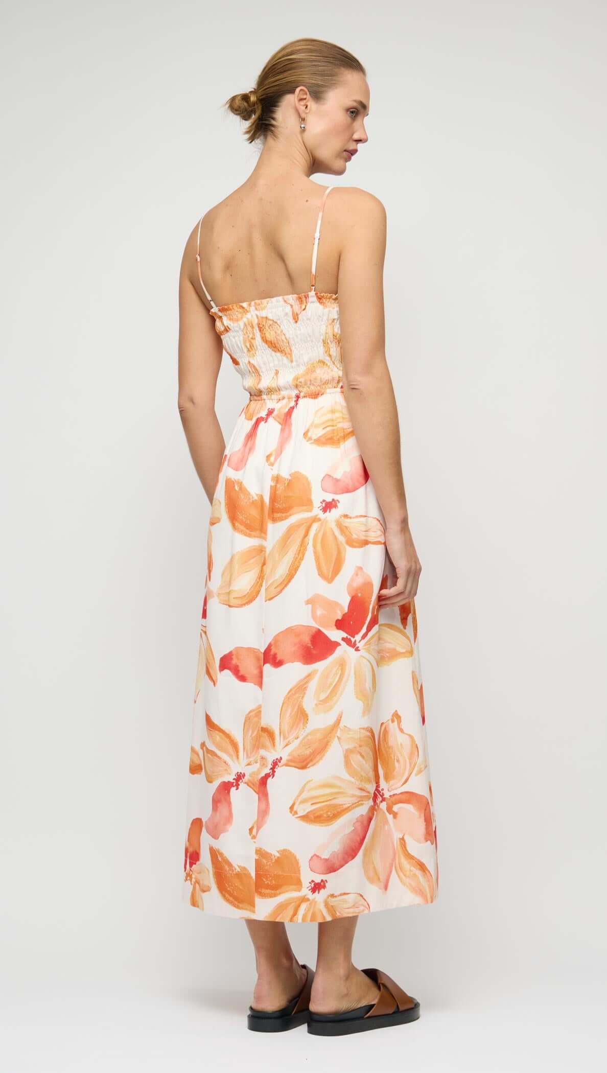 Back view of a woman wearing the Orange & White Floral Shirred Midi Dress with a floral design.