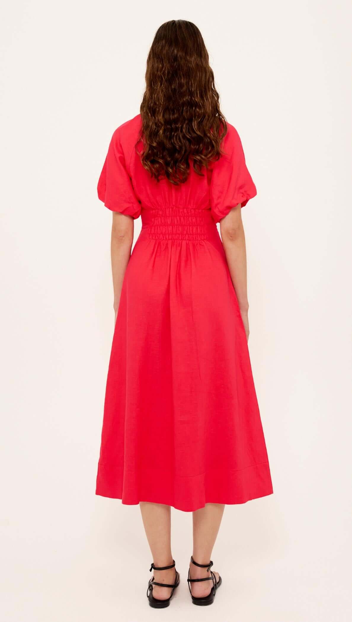 Back view of a woman wearing a Red Linen Blend v-Neck Midi Dress with puff sleeves and a shirred waist.