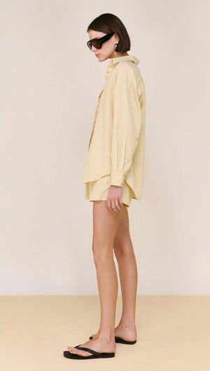 Model wearing a Butter Yellow Striped Shirt styled with sunglasses and shorts, showcasing a relaxed silhouette.