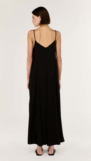 Back view of a woman wearing a Black V-Neck Floaty Maxi Dress with fine shoulder straps and a fluid silhouette.
