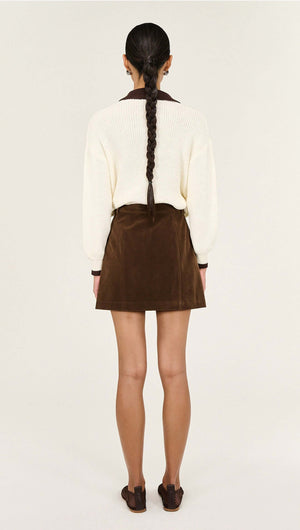 Back view of a model wearing a Brown Vegan Suede Mini Skirt with a cream sweater and braided hair.
