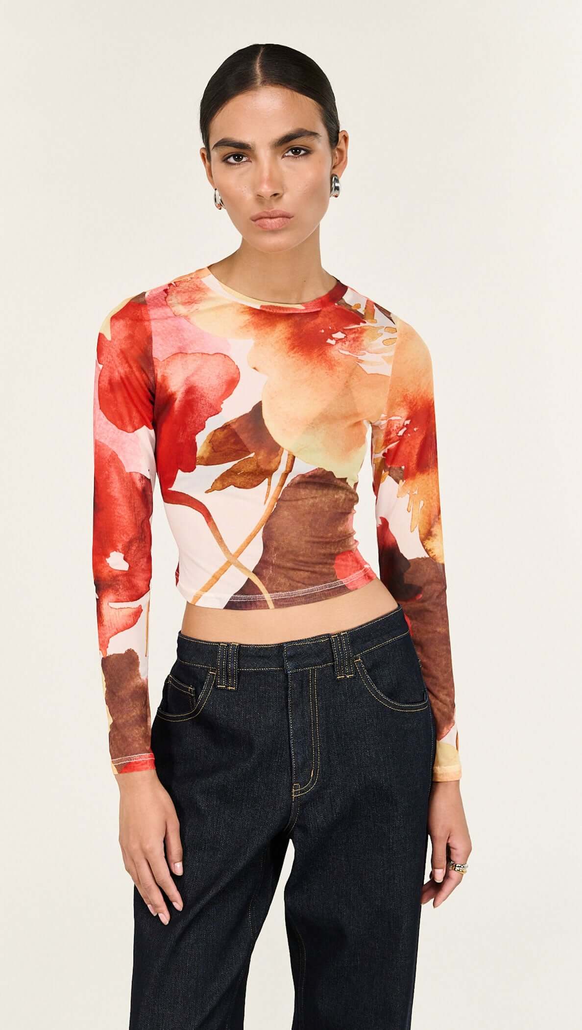 Model wearing the Burnt Floral Long Sleeve Mesh Top, featuring a watercolor floral design with a cropped fit.