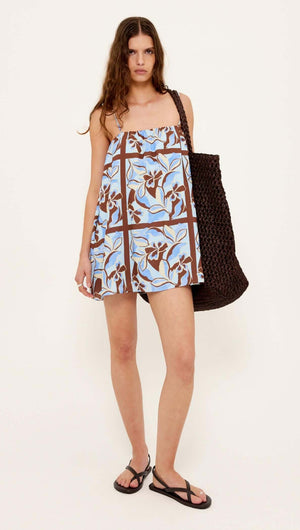 Model wearing a Blue Abstract floral Mini Dress with gathered neckline and adjustable straps, paired with a woven bag.