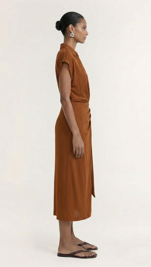 Side view of a model wearing the Copper Draped Wrap Midi Dress in a warm copper hue, showcasing its elegant silhouette.
