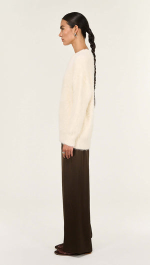 Side view of a model wearing the Cream Fluffy Oversized Jumper with brown pants.