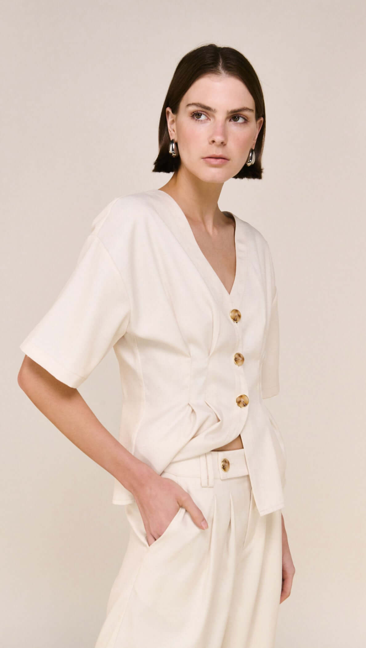 Model wearing a Cream Pintuck Button Front Top with V-neckline and button detailing.