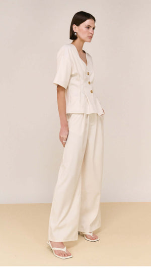 Model wearing Cream Pintuck Button Front Top, featuring a V-neckline and button detailing, paired with wide-leg pants.
