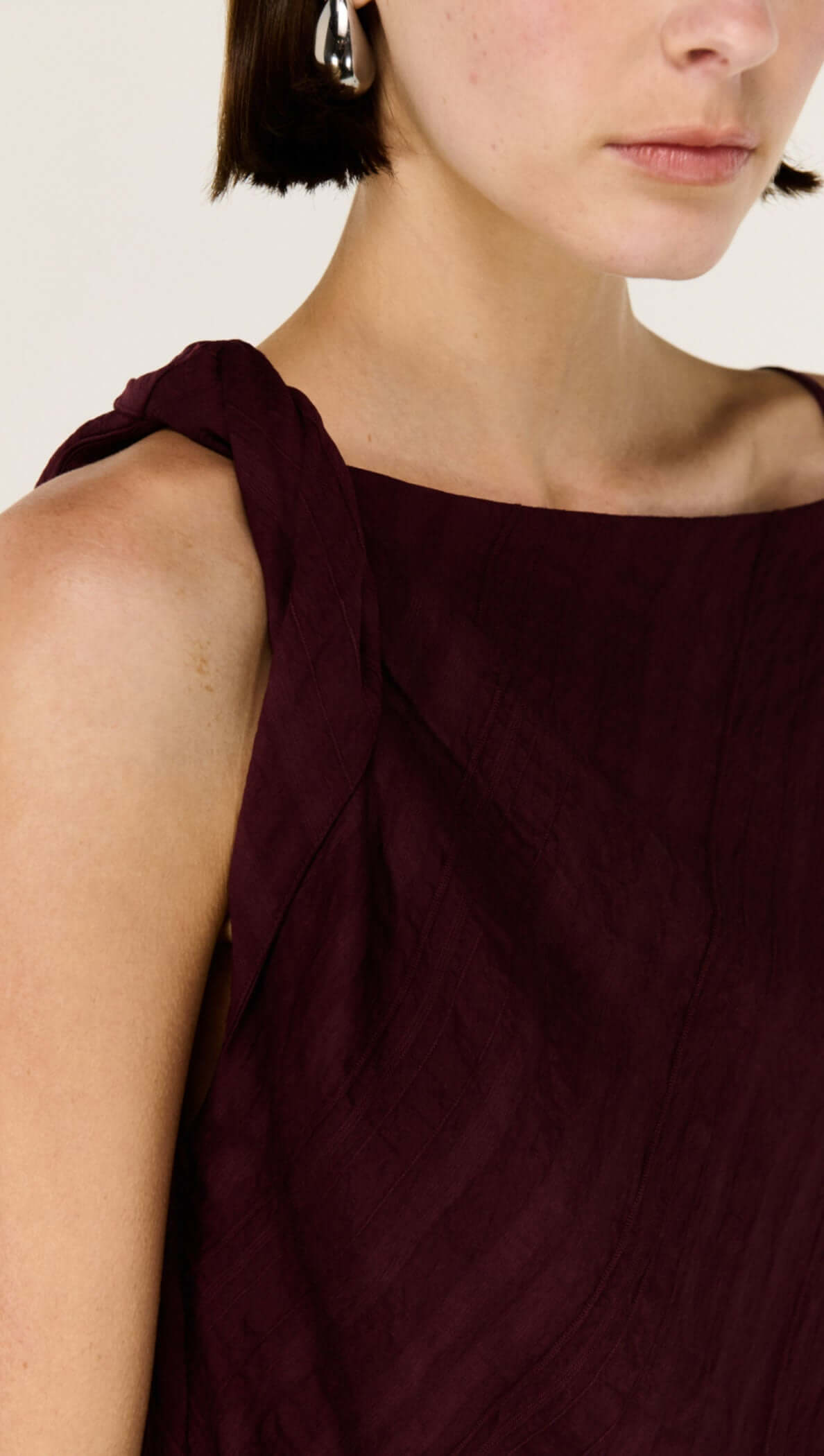 Model wearing Dark Red Textured Asymmetrical Twist Top with asymmetrical neckline and soft drape.