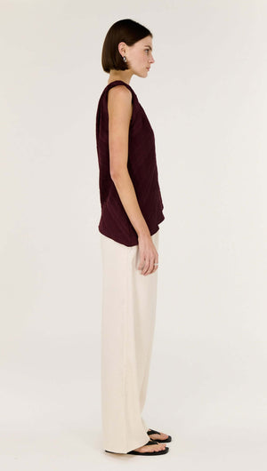 Model wearing a Dark Red Textured Asymmetrical Twist Top with cream-colored pants, showcasing a side view.
