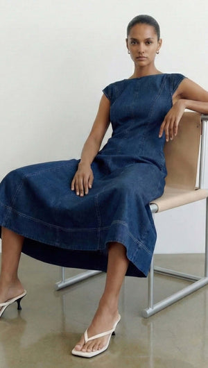 Model wearing Indigo Chambray Panelled Midi Dress seated on a chair, showcasing its stylish design and denim fabric.