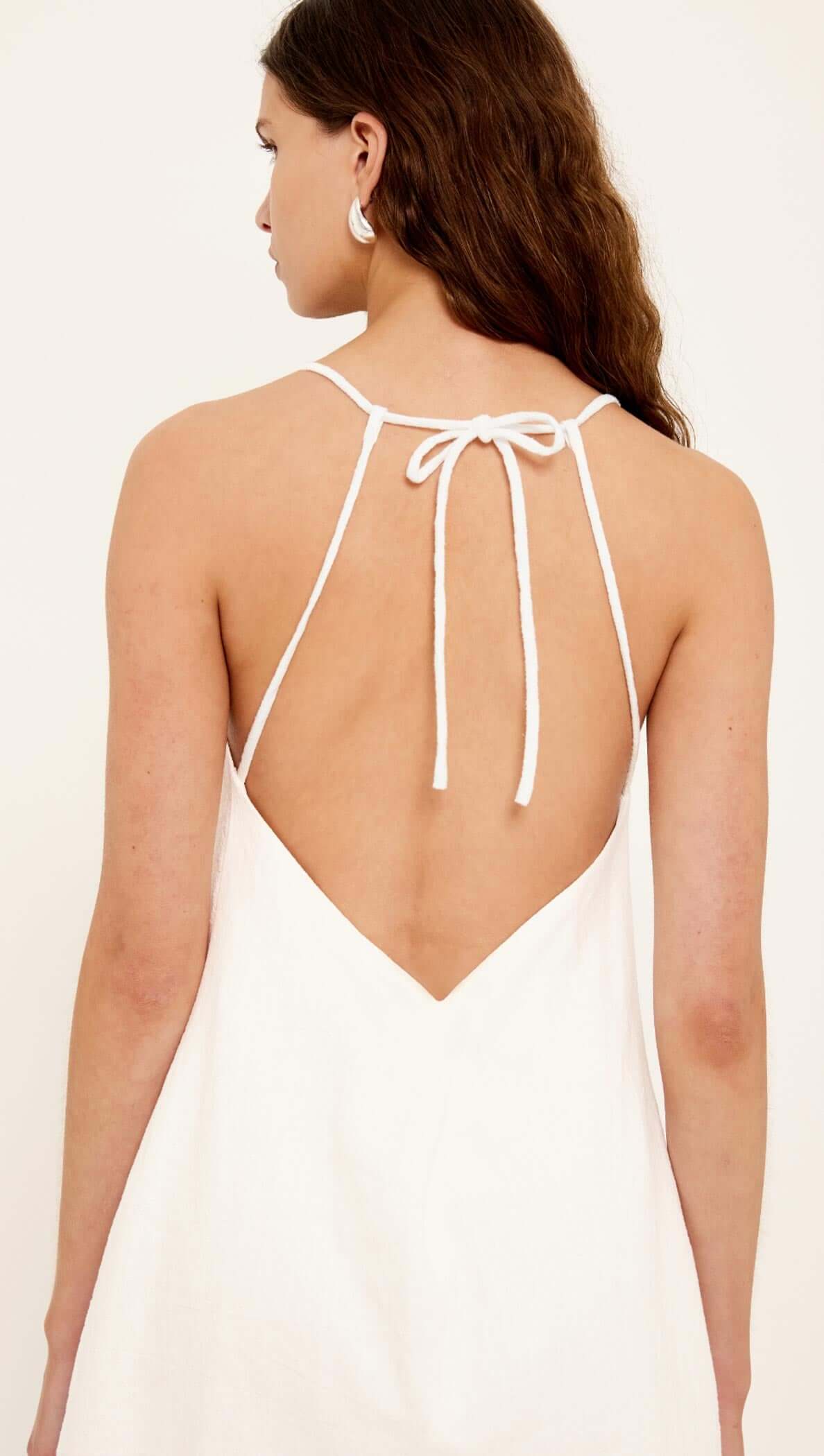 Back view of the Lucia Linen Cotton Blend White Mini Dress showcasing its tie-back straps and relaxed silhouette.