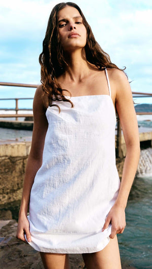 Linen Cotton Blend White Mini Dress worn by a model by the water, showcasing its elegant design and feminine silhouette.