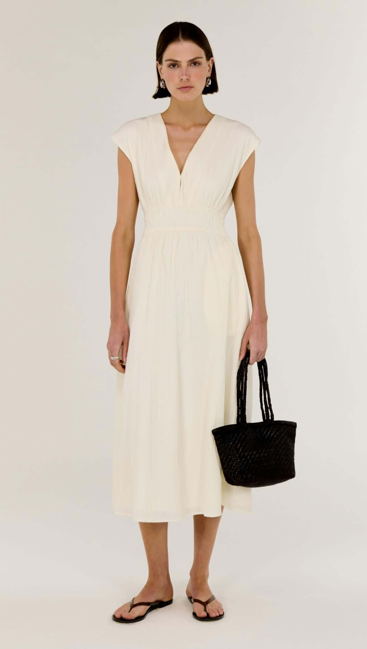 Cream Cotton V-Neck Midi Dress featuring soft cap sleeves and a cinched waist, styled with a black bag.