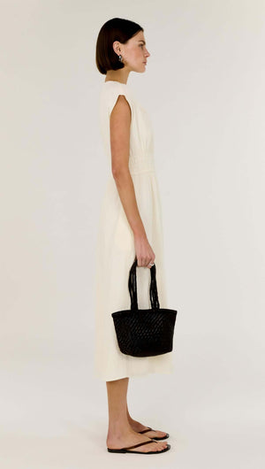Model side view wearing the Cream Cotton V-Neck Midi Dress with cap sleeves, holding a black woven handbag.