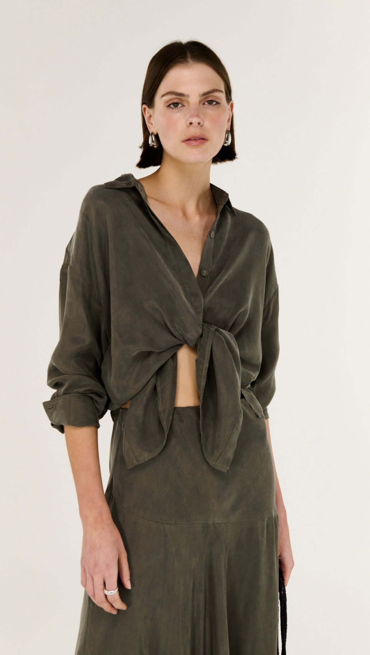 Model wearing an Olive Cupro Oversized Shirt paired with a matching skirt, showcasing modern style and fluid silhouette.