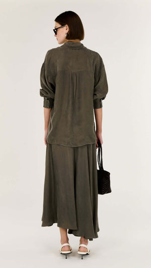 Back view of a model wearing an Olive Cupro Oversized Shirt paired with a matching skirt.