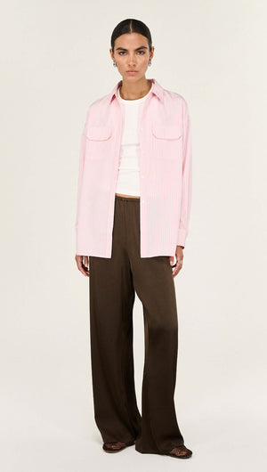 Model wearing a Lina Pink Pinstriped Shirt paired with relaxed brown trousers, showcasing casual style and modern fashion.