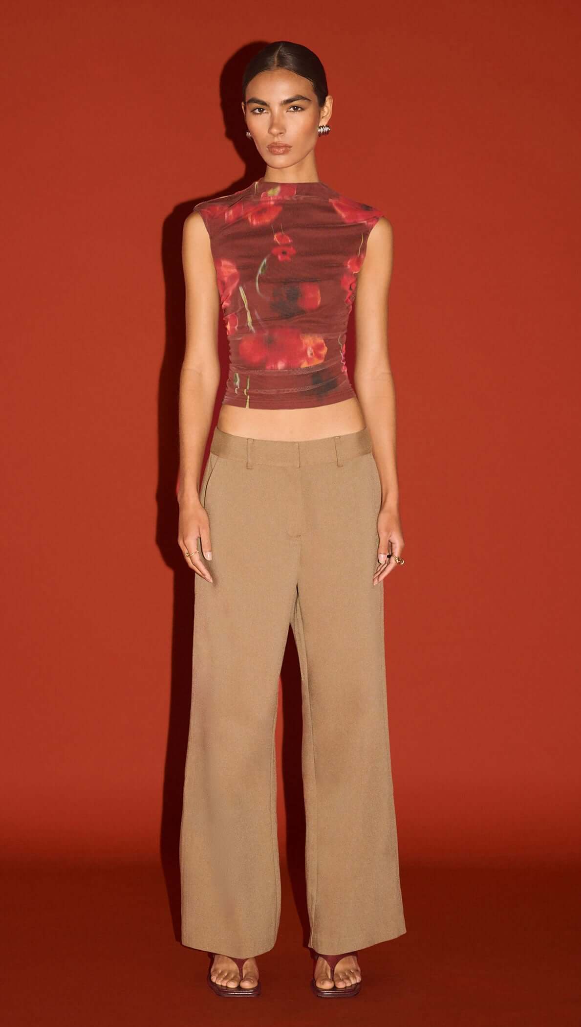 Model wearing a Red Poppy Print Mesh Tank paired with beige wide-leg trousers against a solid red background.