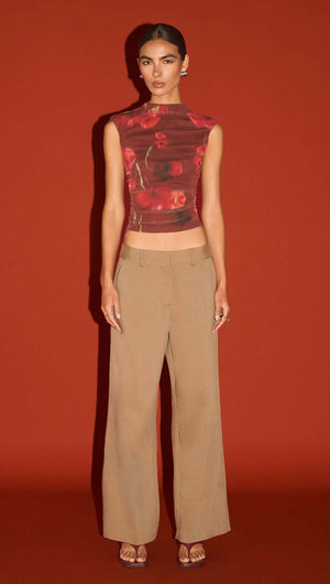 Model wearing a Red Poppy Print Mesh Tank paired with beige wide-leg trousers against a solid red background.