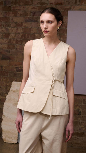 Model showcasing the Stone Cotton Wrap Front Vest in soft ecru, featuring a wrap-front V-neckline and flap pockets.