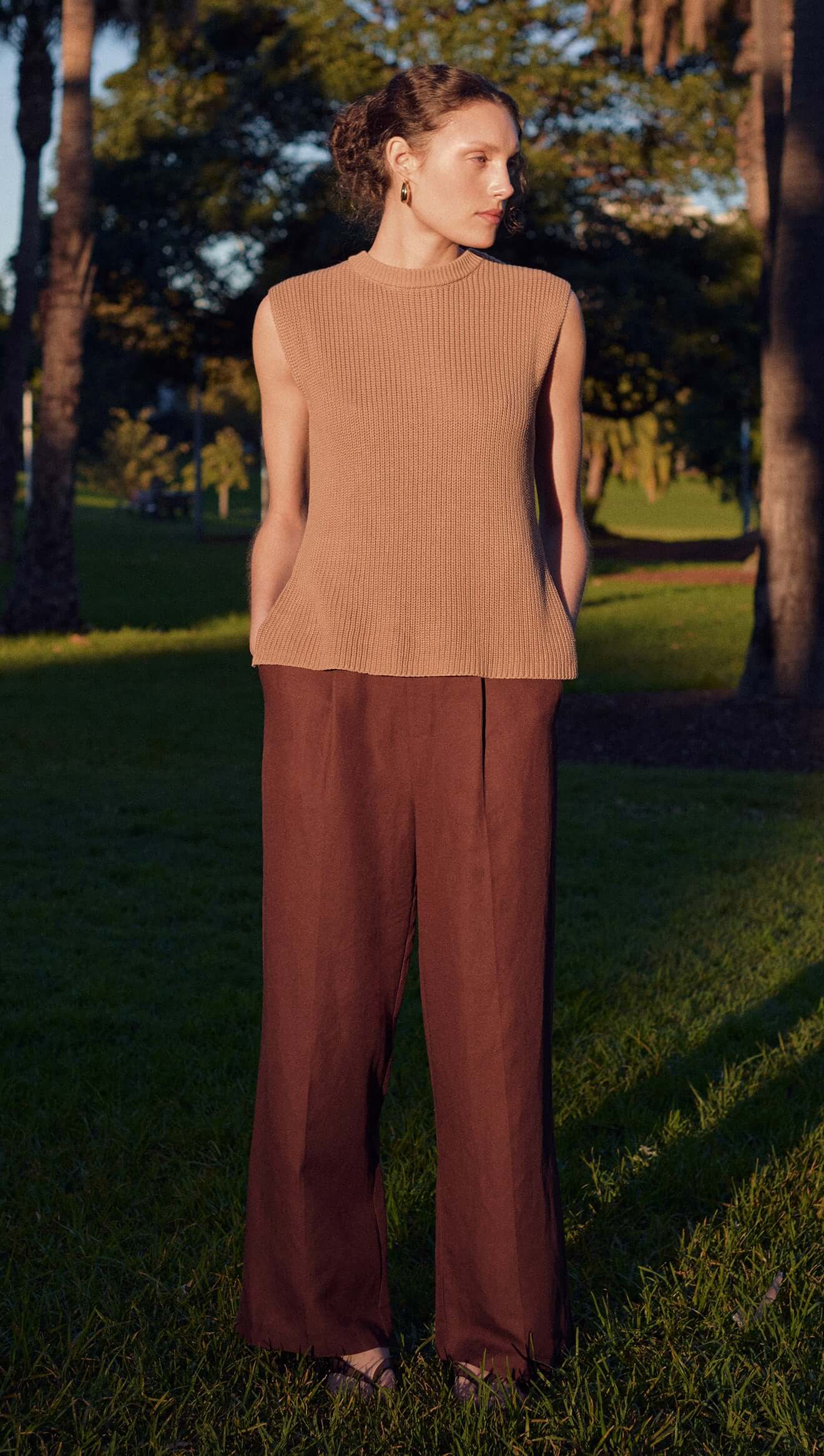 Model wearing a Taupe Cotton Blend Knit Tank Top paired with brown trousers in a sunny outdoor setting.