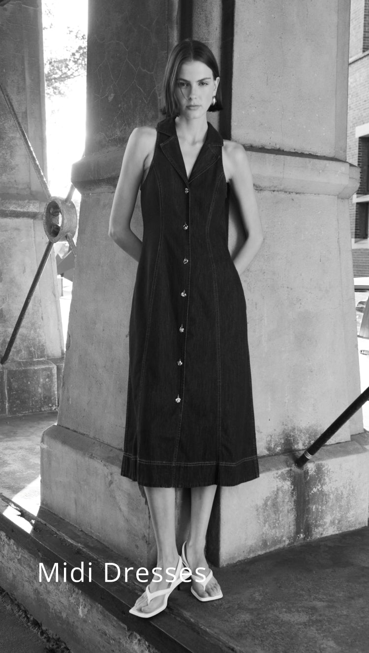 Woman wearing a black sleeveless dress standing against a stone wall.