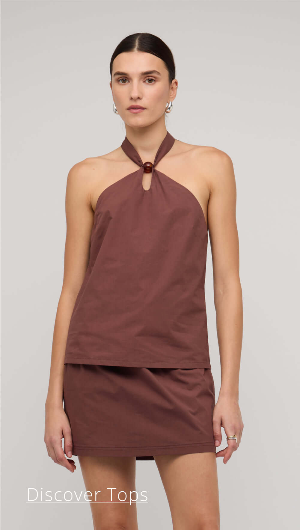 Woman wearing a brown halter top and skirt set on a plain background