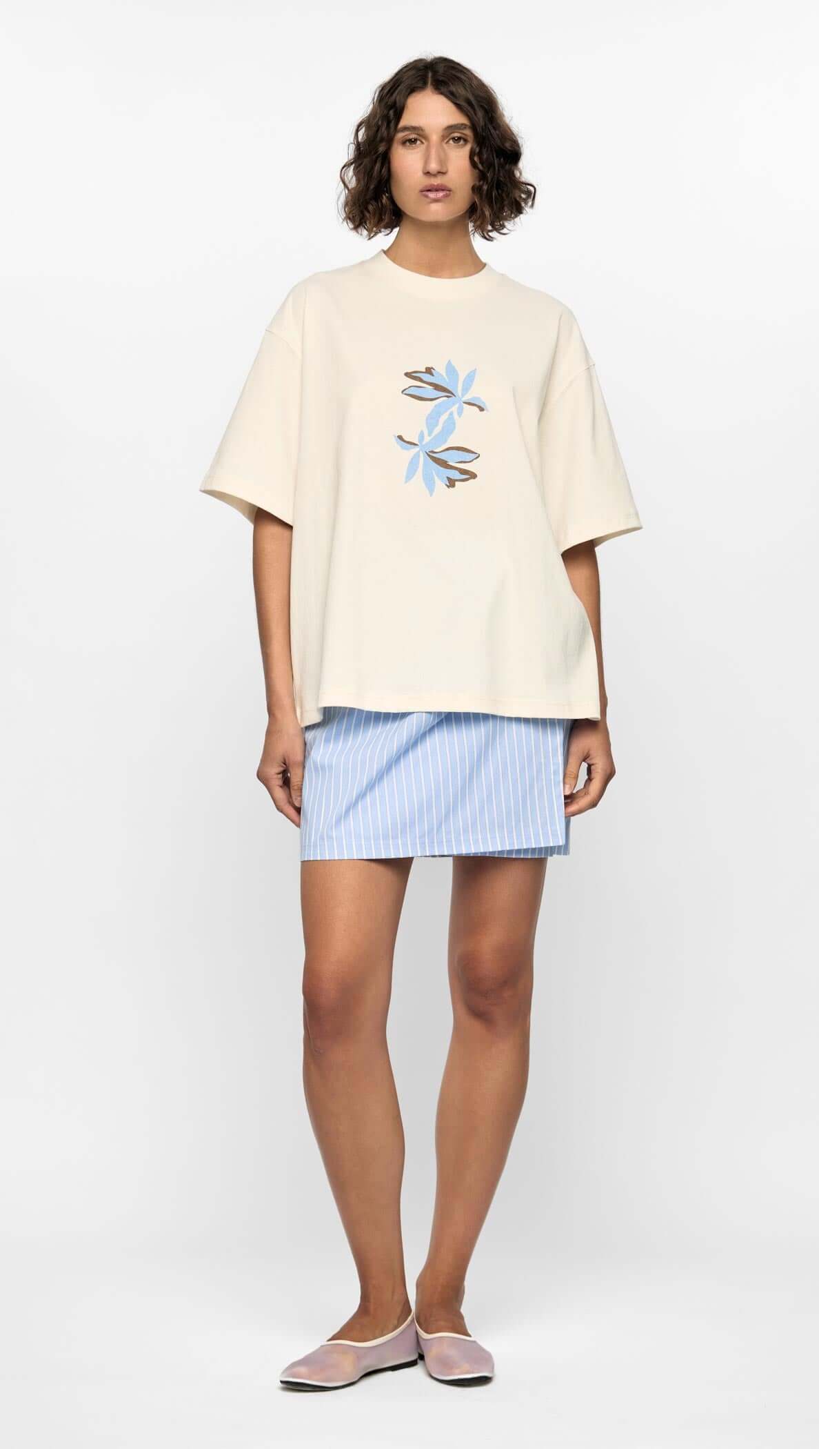 Model wearing the Mae Graphic Tee with abstract blue and brown floral print, styled with a striped skirt.