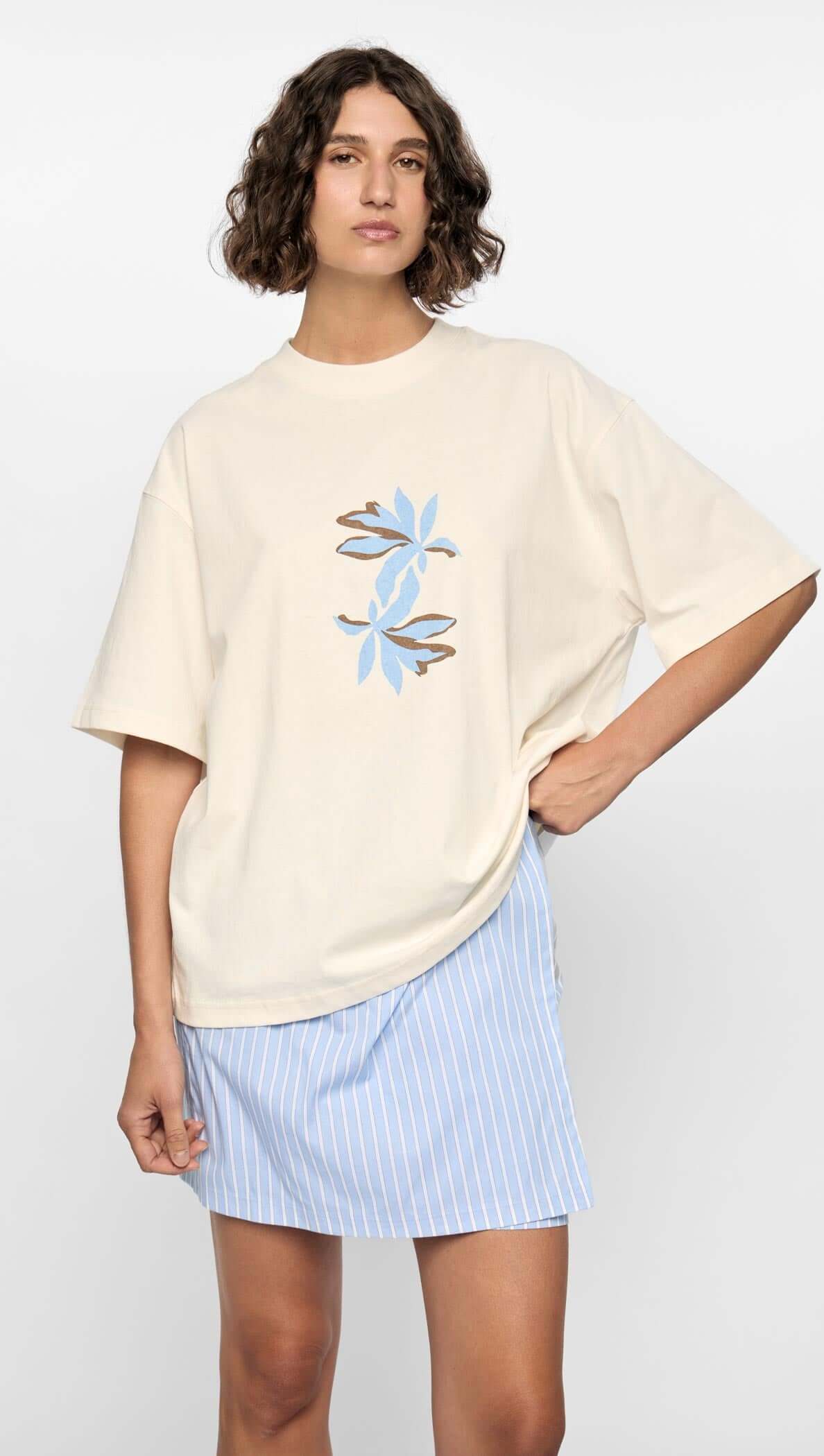 Model wearing a cream oversized t-shirt with floral design and a blue striped mini skirt.