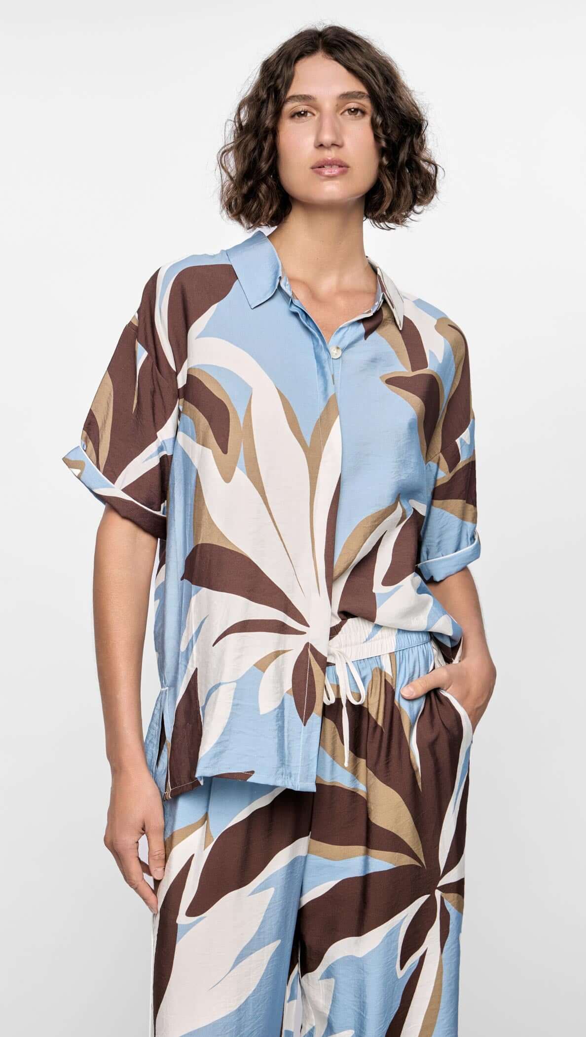 Model wearing the Maeve Resort Shirt with bold abstract print in chocolate, blue, and cream tones, featuring short sleeves and collared neckline.