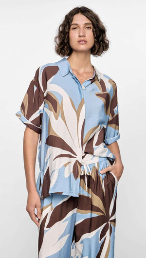 Model wearing the Maeve Resort Shirt with bold abstract print in chocolate, blue, and cream tones, featuring short sleeves and collared neckline.