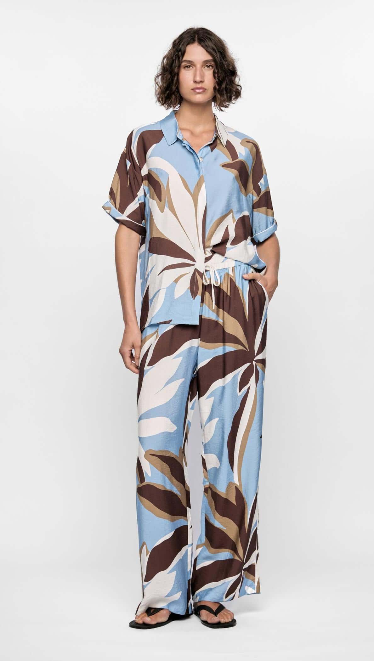 Model wearing the Maeve Resort Shirt with a bold abstract print in brown, blue, and cream, styled casually for summer.