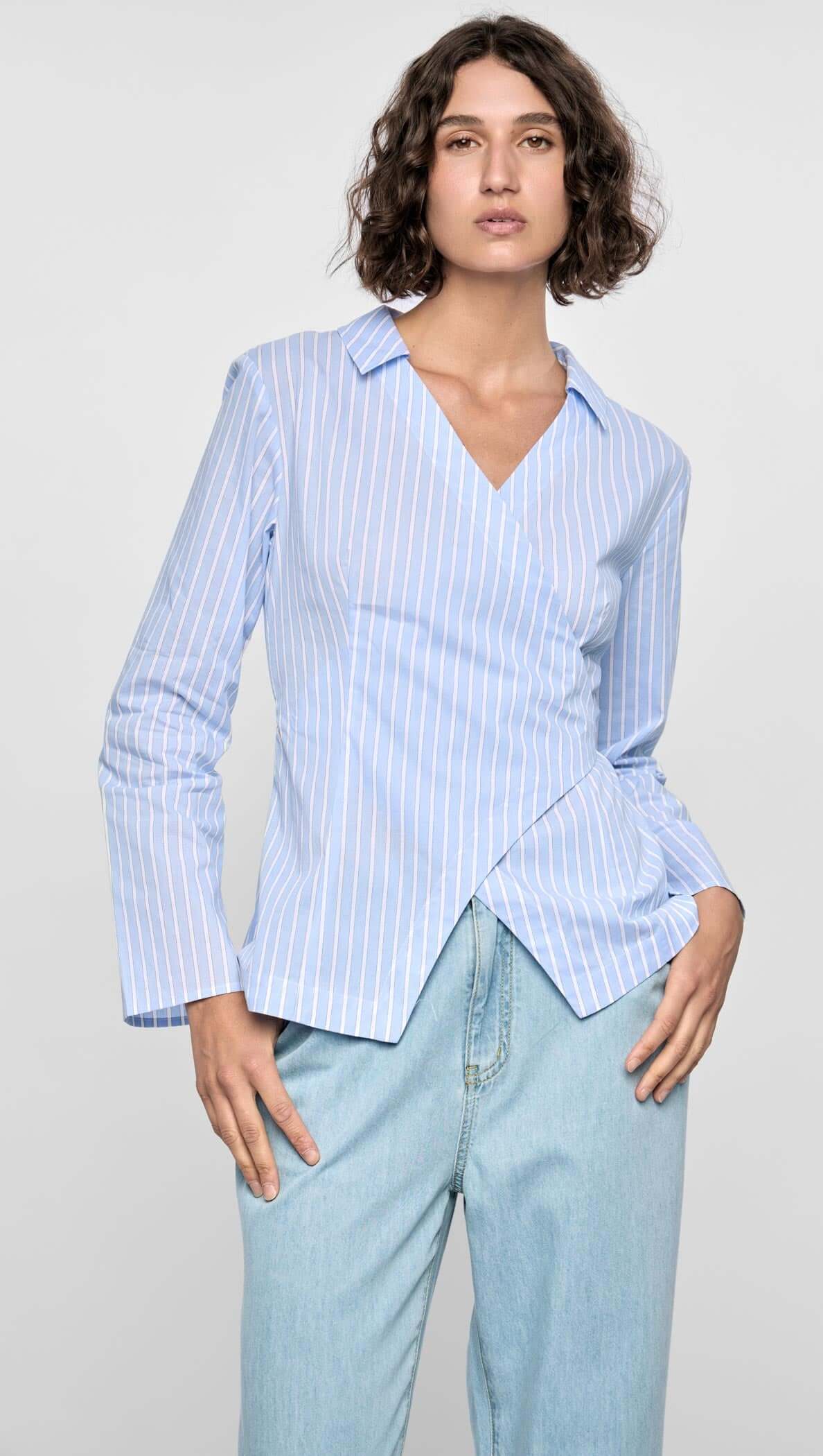 Light blue pinstripe wrap top with asymmetric front, collared neckline, and long sleeves, paired with denim jeans.