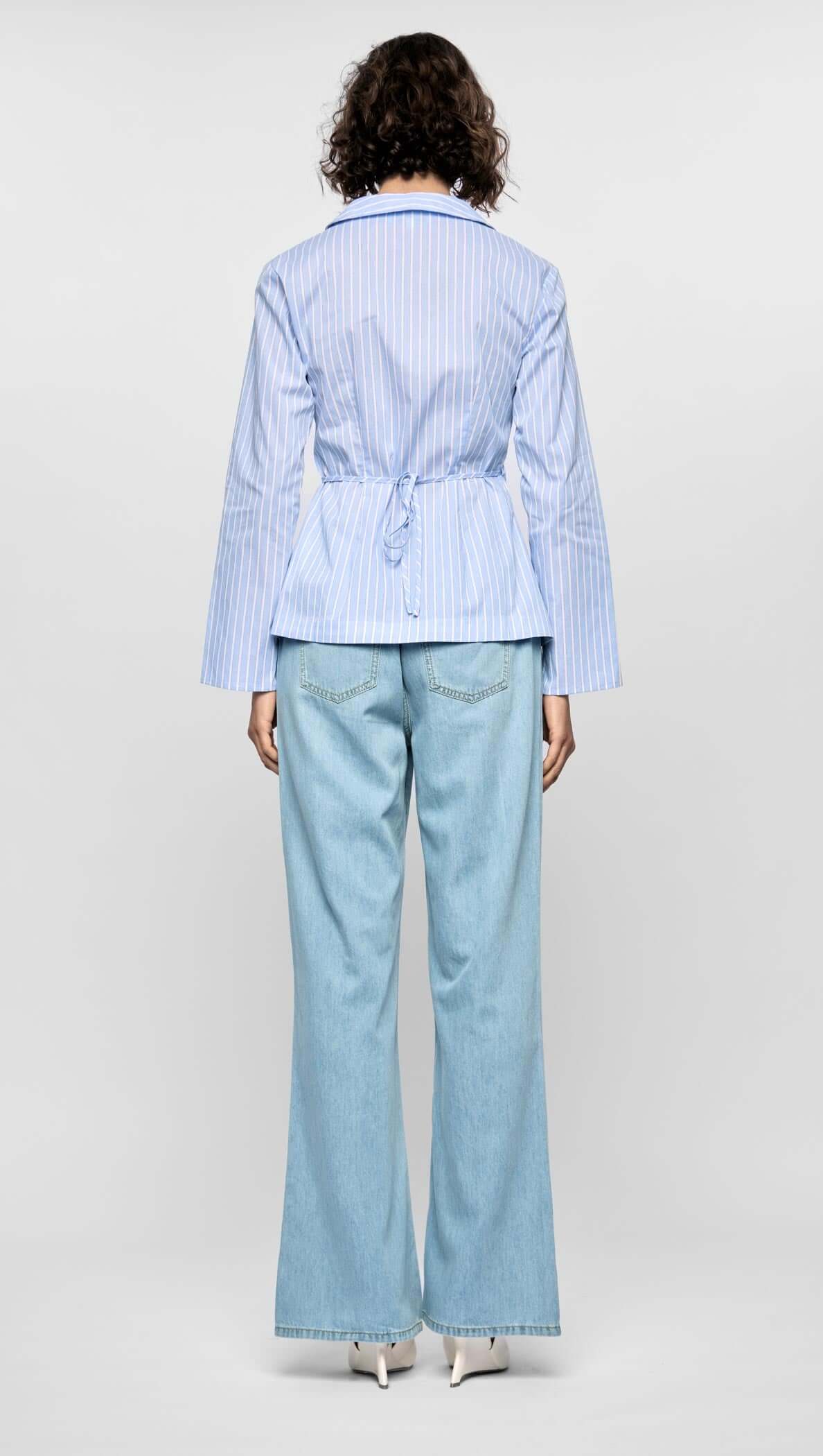 Back view of the Ayra Pinstripe Wrap Top in light blue stripes, paired with wide-leg denim trousers, showcasing a cinched silhouette.