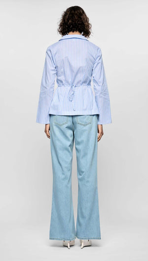 Back view of the Ayra Pinstripe Wrap Top in light blue stripes, paired with wide-leg denim trousers, showcasing a cinched silhouette.