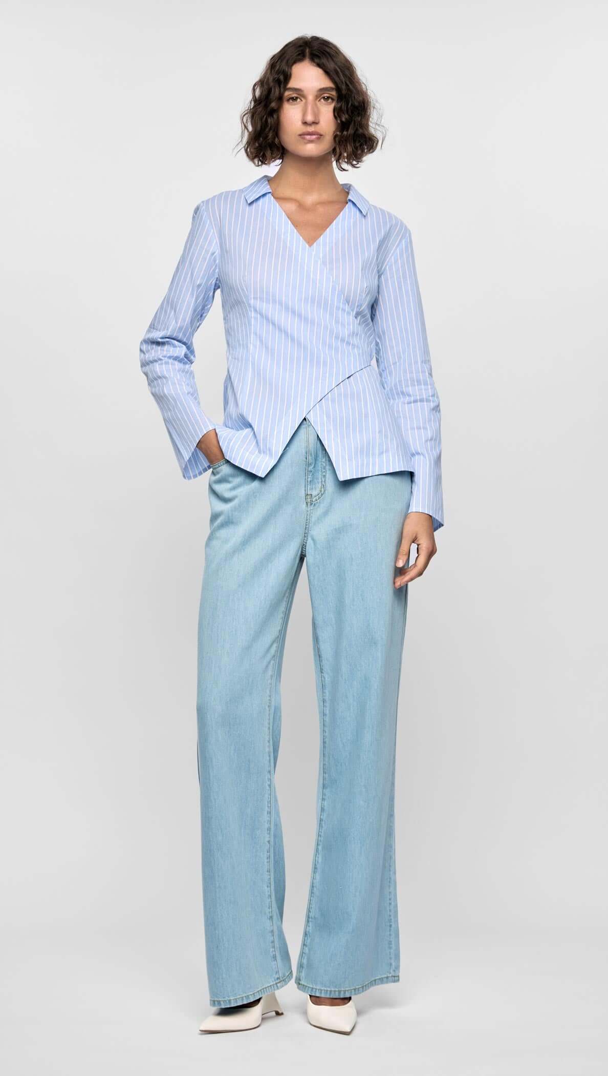 Model wearing the Ayra Pinstripe Wrap Top with light blue stripes, paired with wide-leg denim jeans.