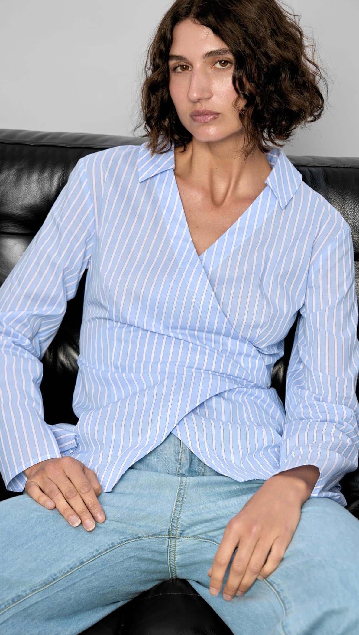 Model wearing the Ayra Pinstripe Wrap Top, featuring light blue stripes and a stylish asymmetric front wrap.