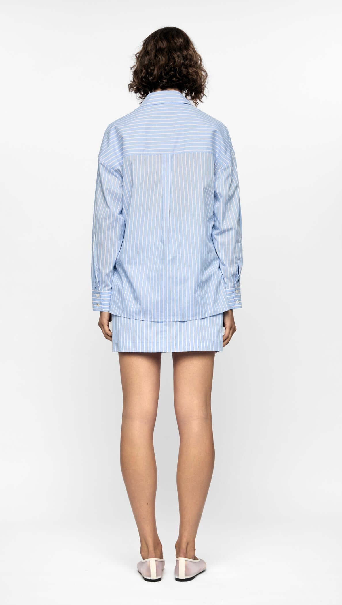 Back view of a model wearing a blue striped Ayra shirt with relaxed fit and modern hem.