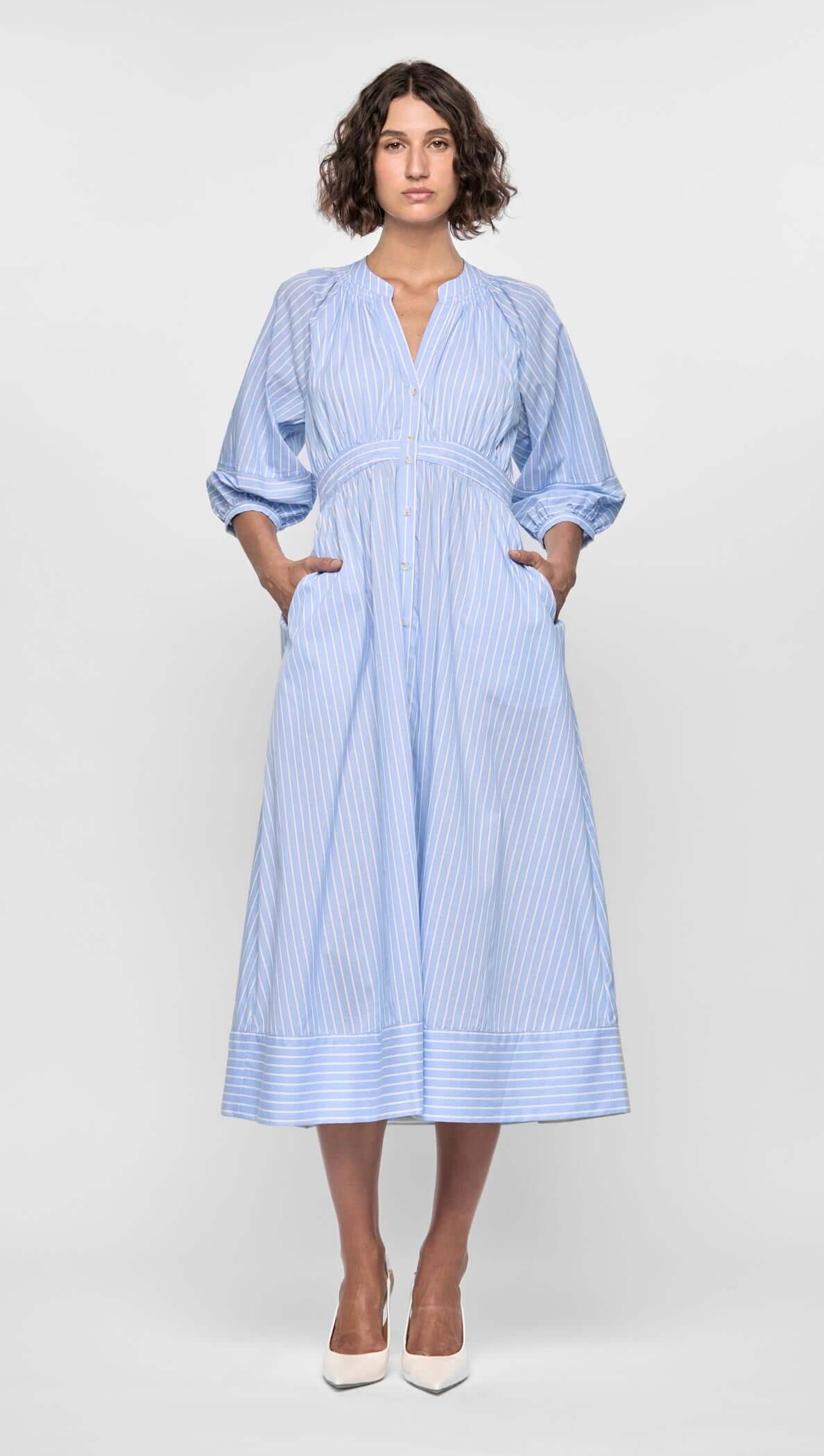 Woman wearing the Myra Midi Dress featuring soft blue pinstripes, puff sleeves, and a flattering empire waist.
