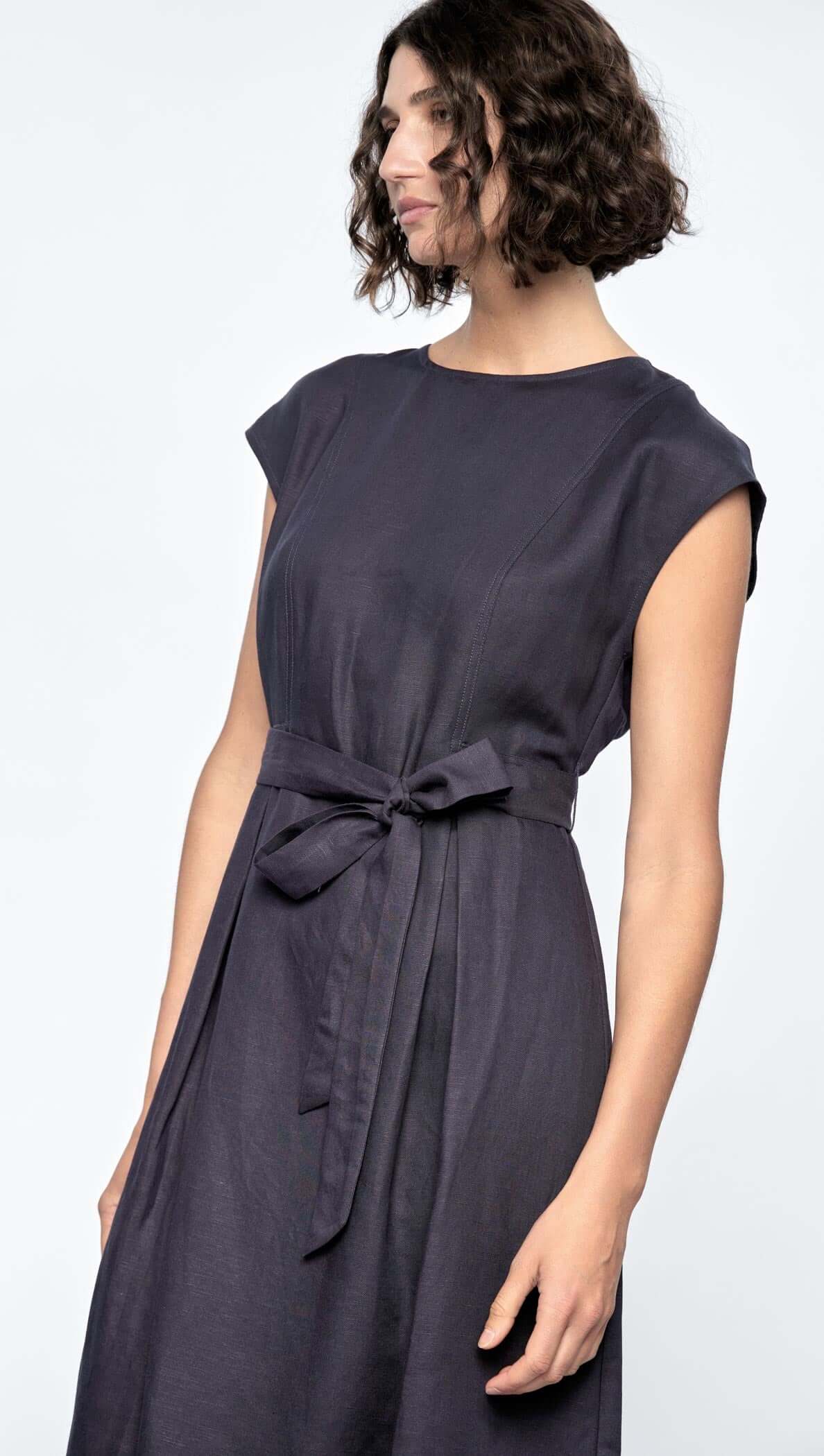 Model in a sleeveless Rhea Midi Dress, featuring a self-tie belt, deep navy color, and cap sleeves.