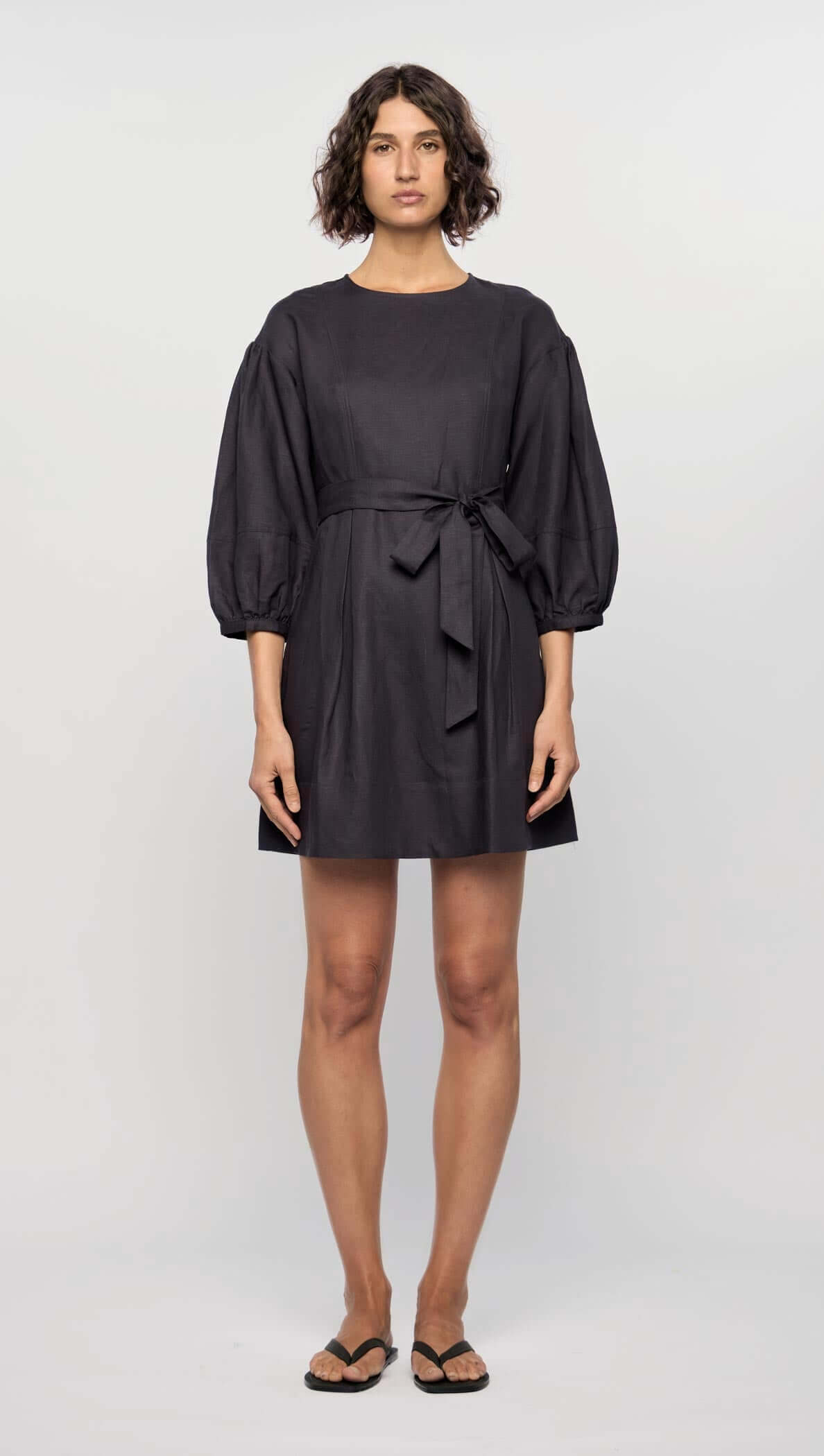 Model wearing the Rhea Mini Dress in navy, featuring 3/4 puff sleeves, a waist tie, and a flattering A-line silhouette.
