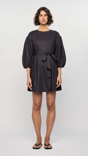 Model wearing the Rhea Mini Dress in navy, featuring 3/4 puff sleeves, a waist tie, and a flattering A-line silhouette.