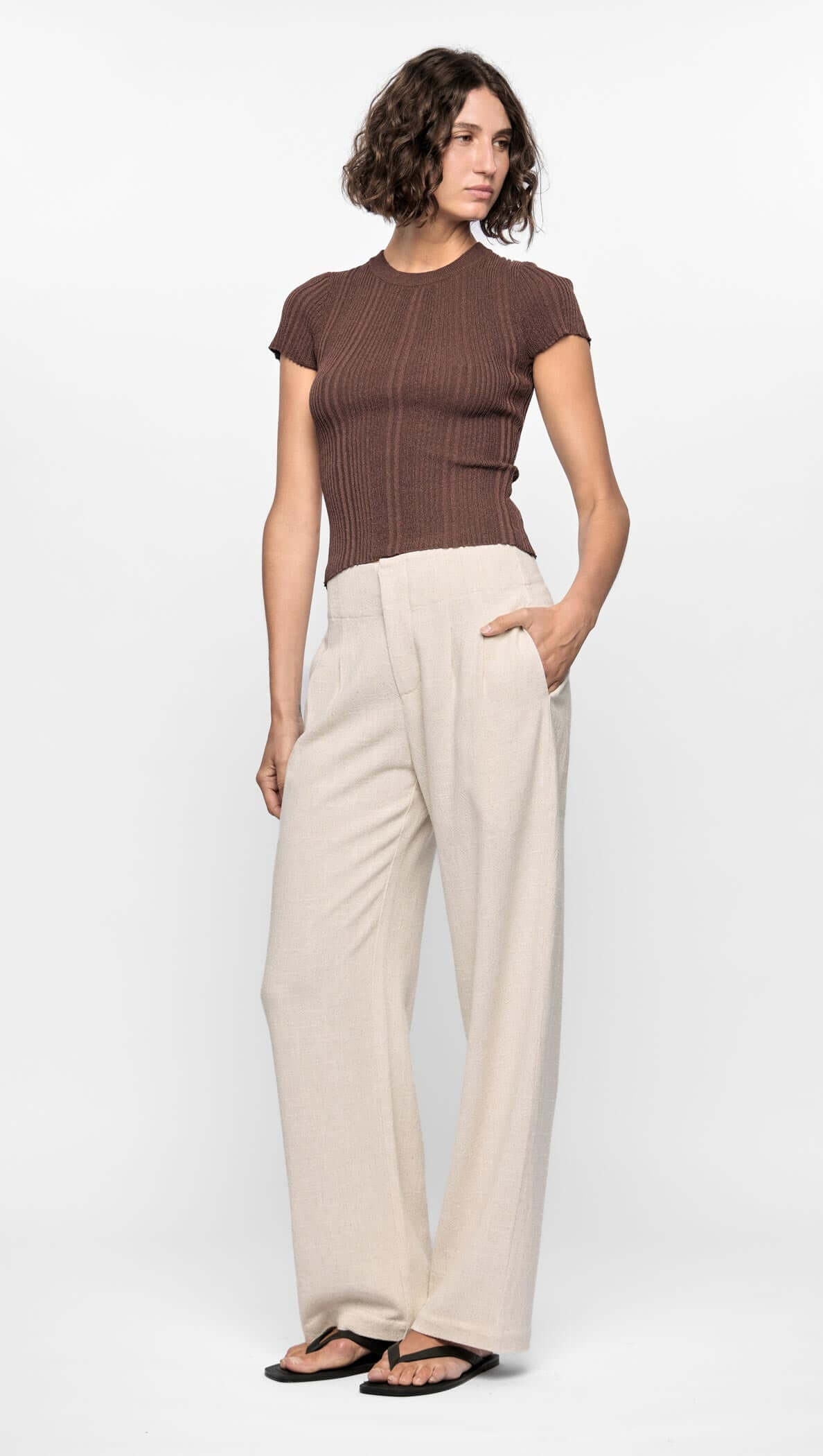 Maya Ribbed Knit Tee in rich chocolate brown paired with cream wide-leg trousers on model with tousled hair.