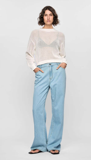 Model wearing the Oslo Knit Jumper in off-white, featuring an open-knit texture and relaxed fit, paired with blue jeans.